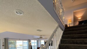 Amplia sala de estar con escalera alfombrada, ventilador de techo y vista a un balcón.