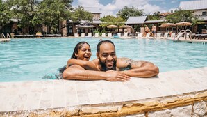 Una piscina con sillas de descanso y sombrillas, rodeada de edificios y árboles.