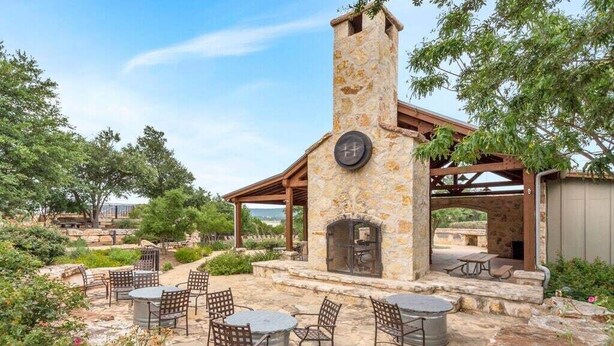 Un patio al aire libre con mesas y sillas de piedra, una chimenea de piedra y una estructura de pérgola.