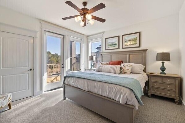 A bedroom with a bed, a nightstand, a ceiling fan, and a view of the outdoors through a door.