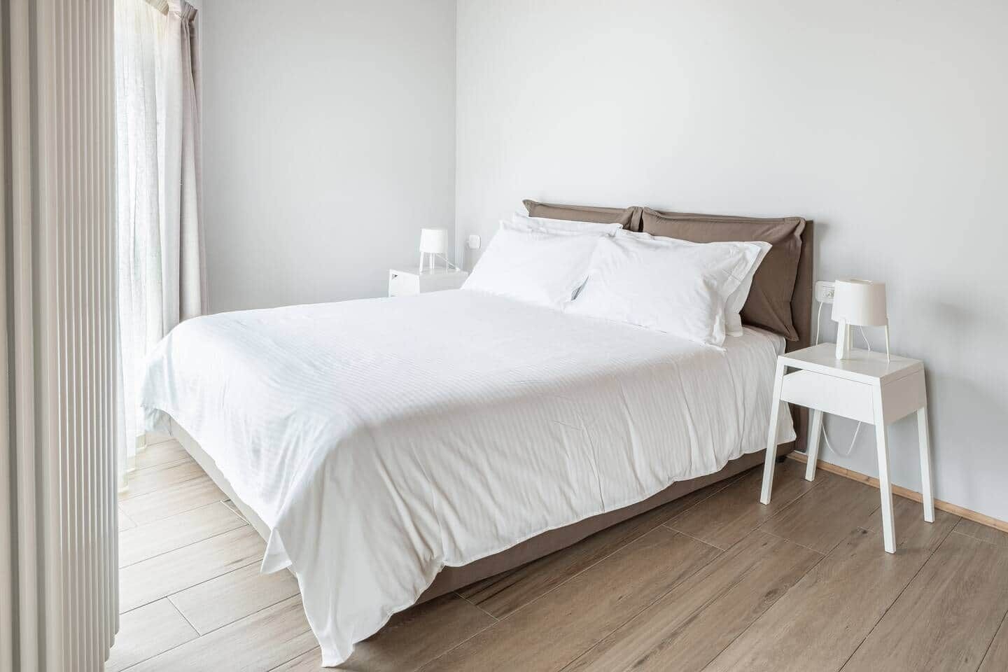 Una camera da letto con un letto, comodini bianchi, una lampada da comodino e una finestra con tende.
