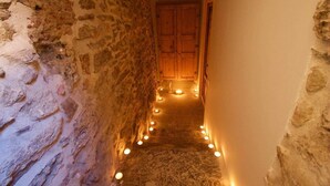 Un étroit couloir en pierre, avec une porte en bois au bout, éclairé par de petites lampes disposées le long du passage.