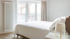 Une chambre à coucher avec un lit, un radiateur, une fenêtre avec des rideaux et une vue sur un bâtiment à l’extérieur.