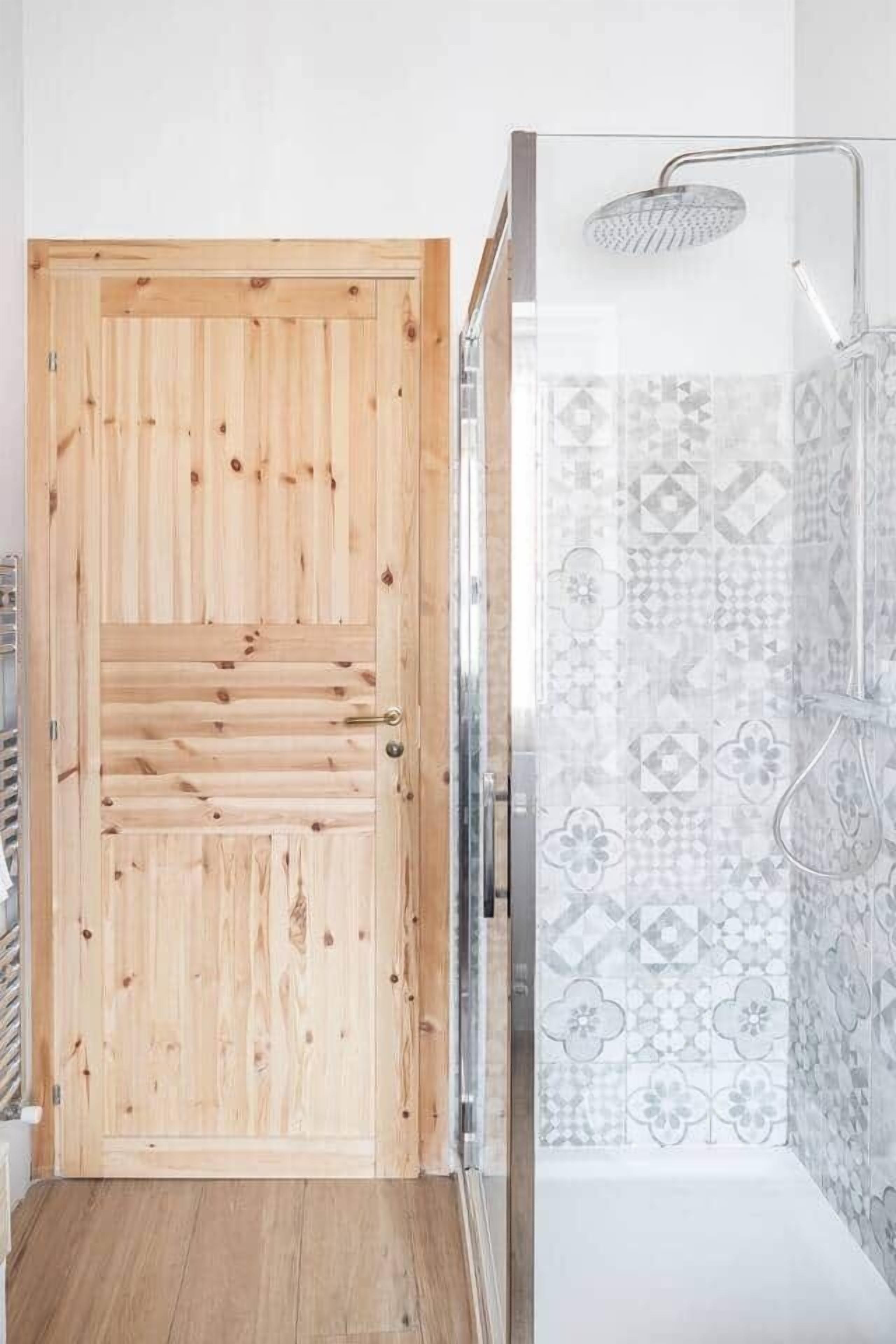 A wooden door with a glass panel, a shower with a patterned tile wall, and a metal showerhead.