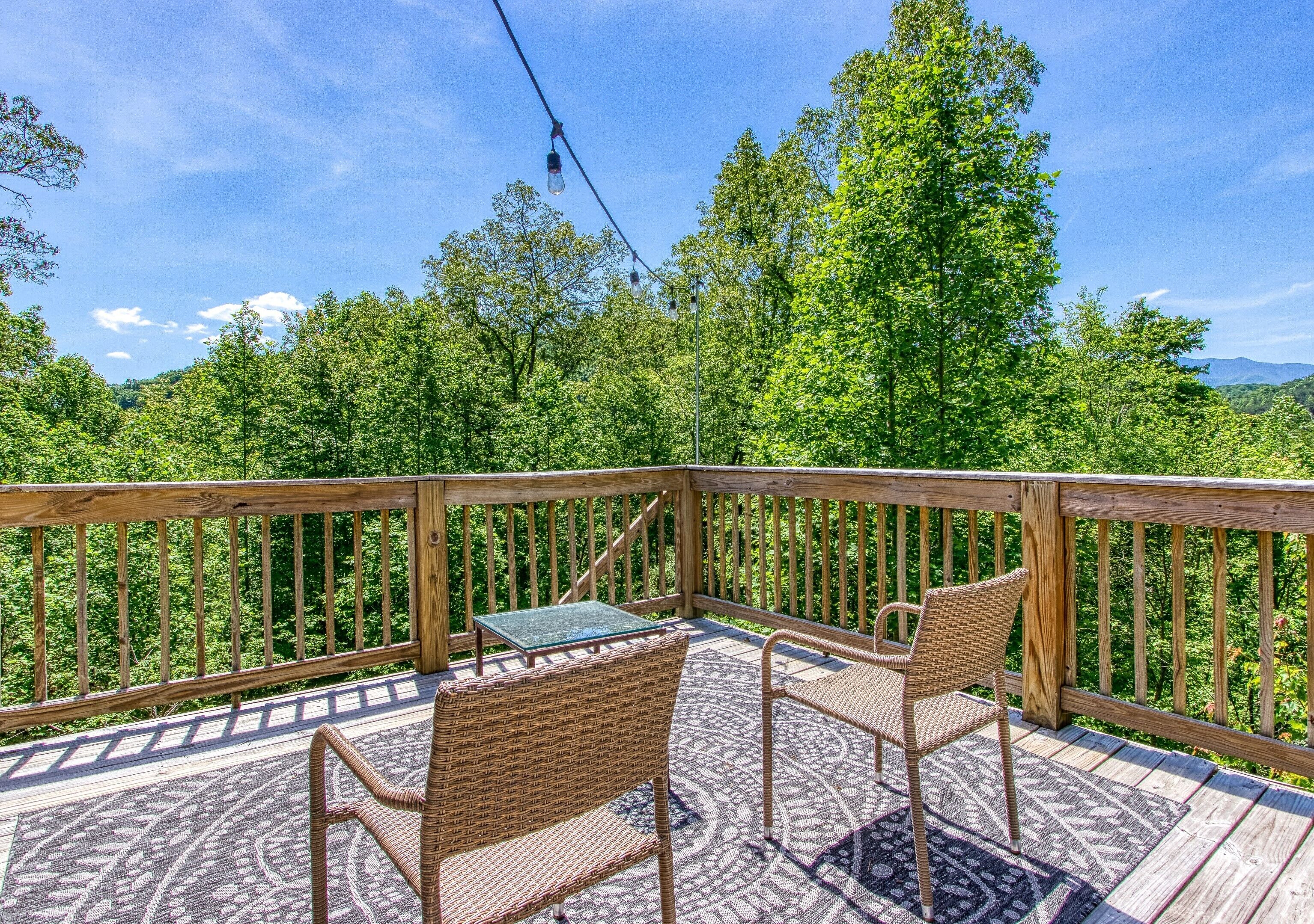 A wooden deck with wicker furniture and a glass table, overlooking a forested area.