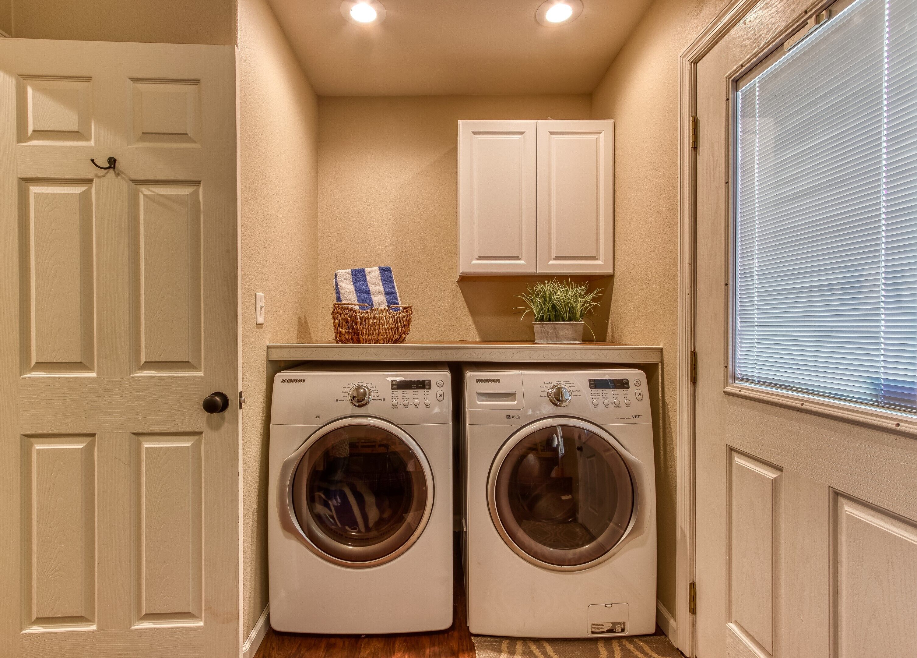 A laundry room with two front-loading washing machines, a basket with a towel, and a potted plant on a shelf.