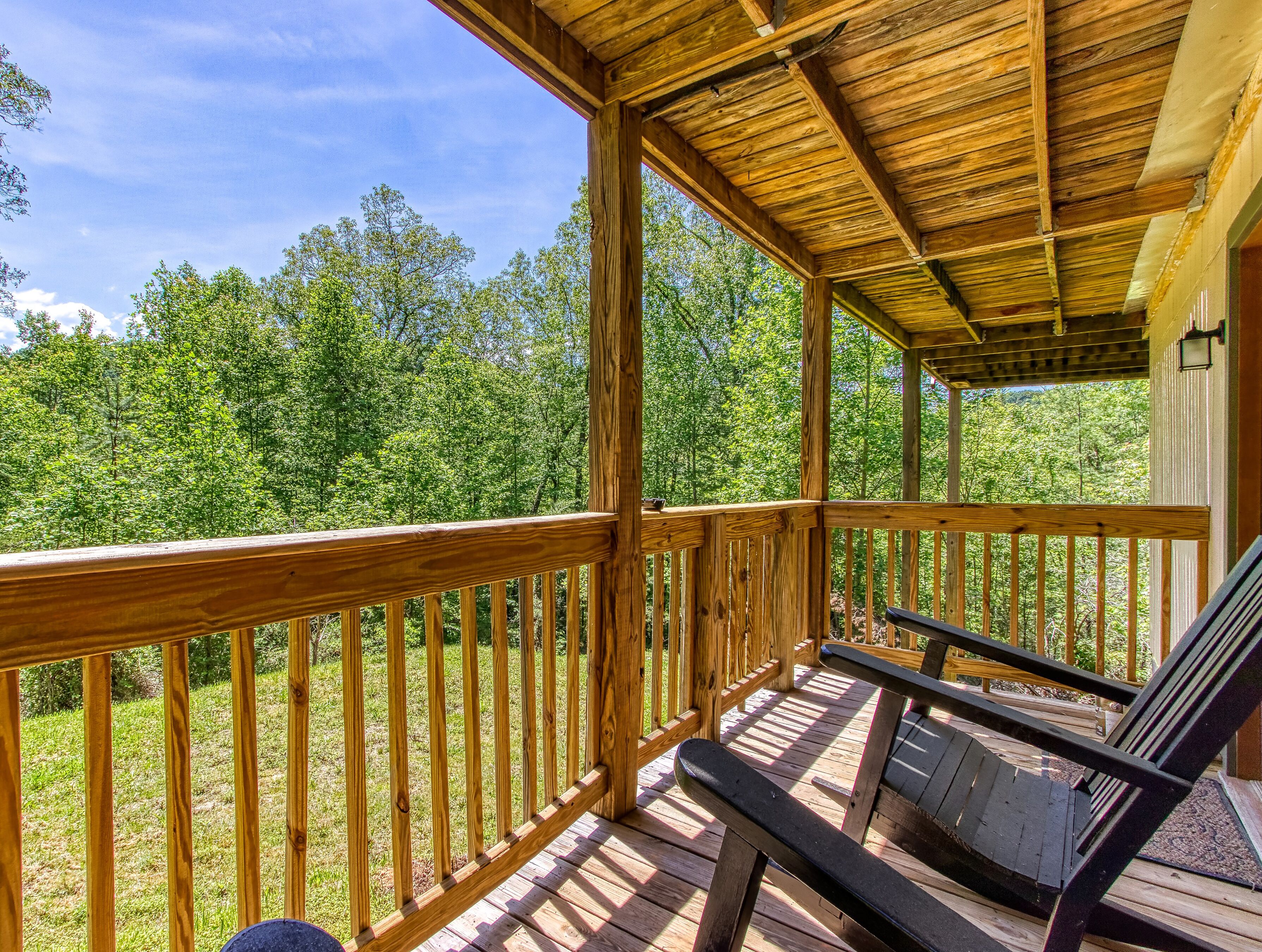 A wooden deck with a railing, benches, and a view of a forest.