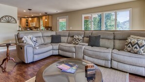 A living room with a sectional sofa, a glass coffee table, and a view of the kitchen. - Deer & Doe by HoneyBearCabins (Sevierville)