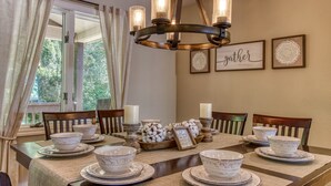A dining area with a table set for four, featuring white bowls and plates, a chandelier, and framed decor on the wall. - Deer & Doe by HoneyBearCabins (Sevierville)