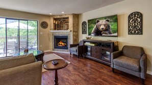 A living room with a fireplace, a large bear painting, and a view of the outdoors. - Deer & Doe by HoneyBearCabins (Sevierville)