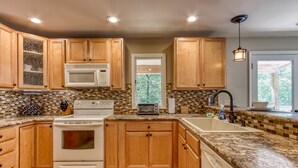 A kitchen with wooden cabinets, a white stove, a microwave, a toaster, and a sink. - Deer & Doe by HoneyBearCabins (Sevierville)