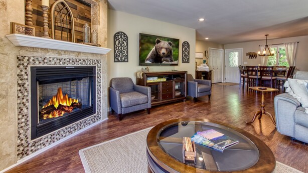 A spacious living room with a fireplace, comfortable seating, and a large bear painting on the wall. - Deer & Doe by HoneyBearCabins (Sevierville)