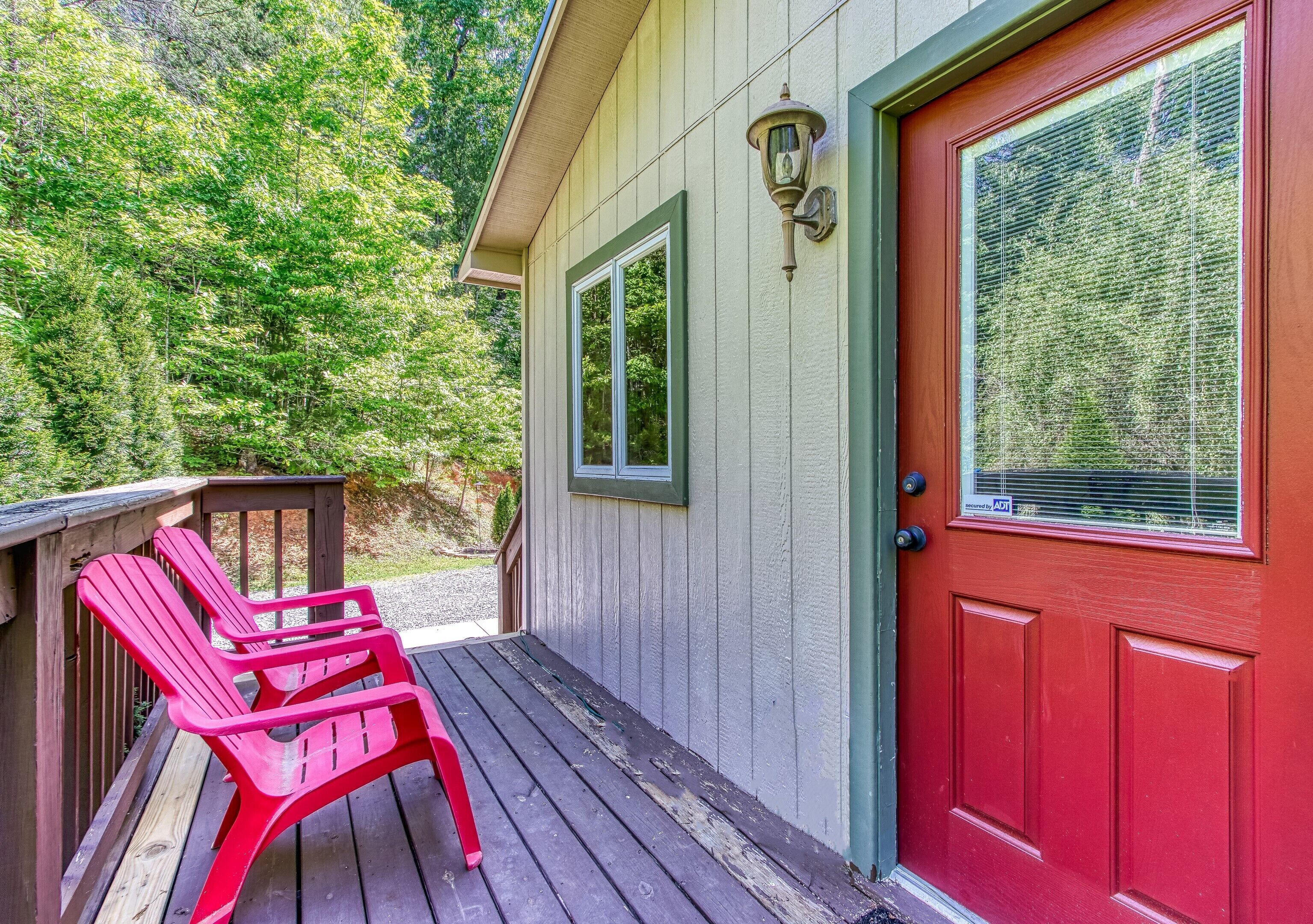 A wooden deck with red Adirondack chairs, a red door, and a window with blinds.