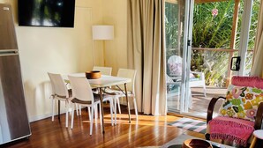 A modern living room with a dining area, a flat-screen TV, a wooden table, and a sofa.