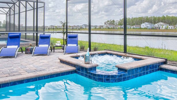 Piscina interna com hidromassagem, espreguiçadeiras e vista para um lago e casas.