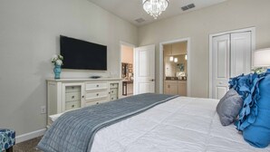 Quarto com cama, cômoda, televisão, lustre e porta para outro ambiente.