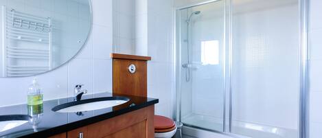 Un baño moderno con tocador de madera, un espejo redondo, cerramiento de ducha de vidrio y un inodoro.