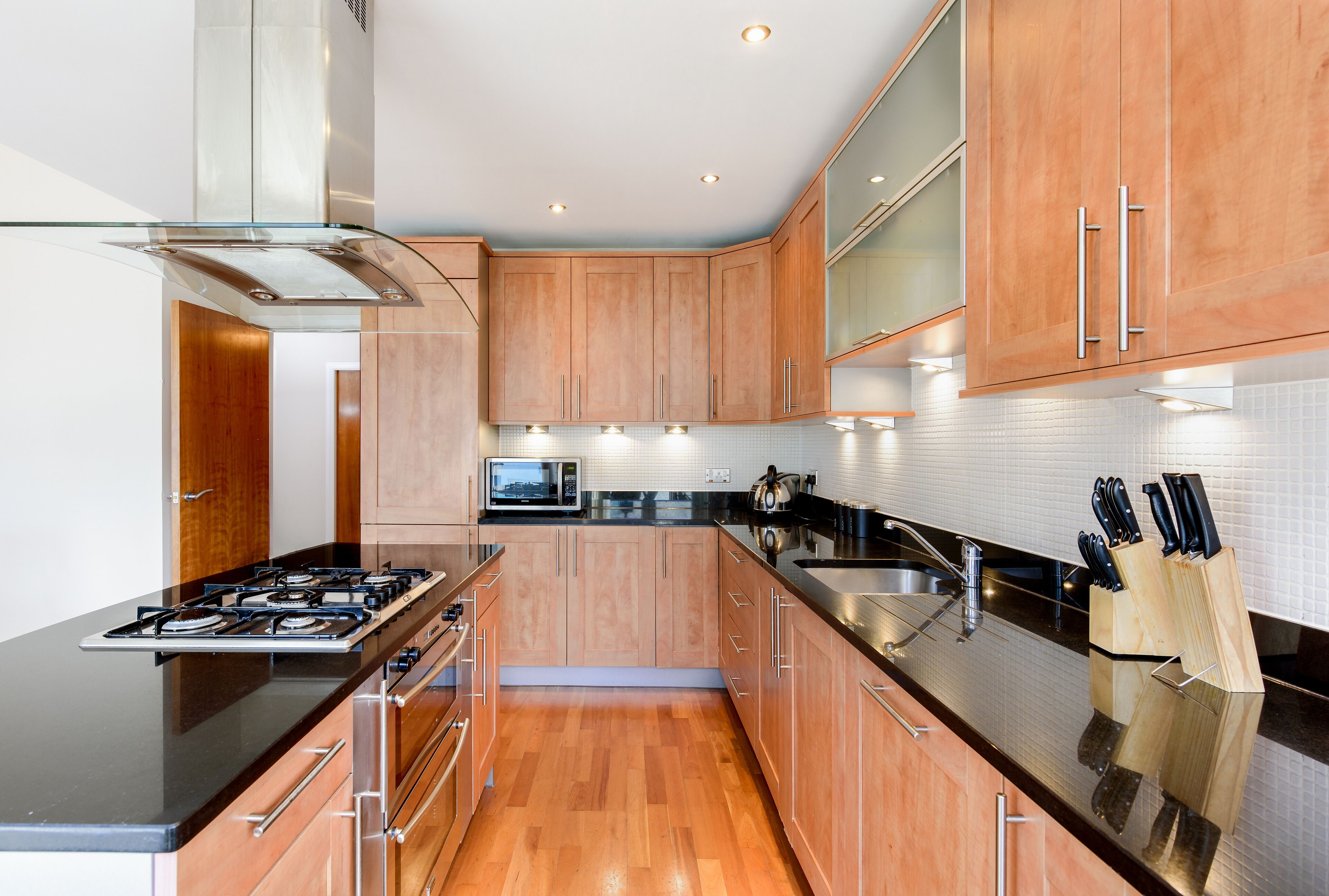 A modern kitchen with wooden cabinets, a black countertop, stainless steel appliances, and a knife block.