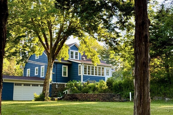 A two-story house with a garage, surrounded by trees and a stone wall.