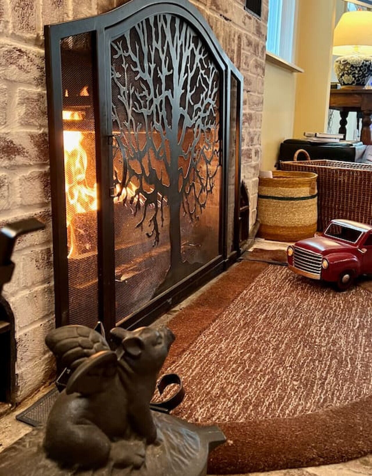 A fireplace with a decorative metal screen, a bear sculpture, and a vintage toy car on a rug.