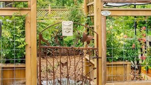 A wooden pergola structure with a star-shaped ornament, a metal gate with decorative elements, and a garden with various plants. - Woodstock Farmhouse /Hot tub, Gardens,EV charger, Firepit, Pet/Family Friendly (Saugerties)