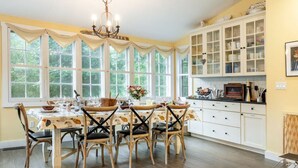 A dining area with a table set for four, surrounded by chairs, and a kitchen with cabinets and a countertop. - Woodstock Farmhouse /Hot tub, Gardens,EV charger, Firepit, Pet/Family Friendly (Saugerties)