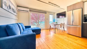 A modern living room with a blue sofa, wooden flooring, a kitchen with a stainless steel refrigerator, and a dining area with a table and chairs. - Suite 216: Beautiful 2-Bedroom Beachfront Suite (Wainfleet)