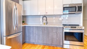 A modern kitchen with stainless steel appliances, a grey wooden countertop, and white cabinets. - Suite 216: Beautiful 2-Bedroom Beachfront Suite (Wainfleet)