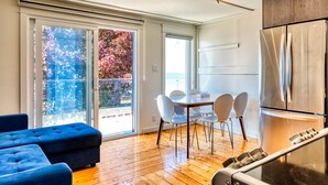A modern kitchen with a stainless steel refrigerator, a dining area with a table and chairs, and a large window with a view of trees. - Suite 216: Beautiful 2-Bedroom Beachfront Suite (Wainfleet)