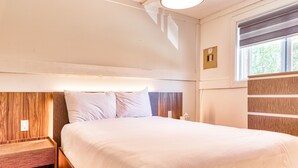 A neatly made bed with a wooden headboard, a bedside table, and a window with blinds. - Suite 216: Beautiful 2-Bedroom Beachfront Suite (Wainfleet)
