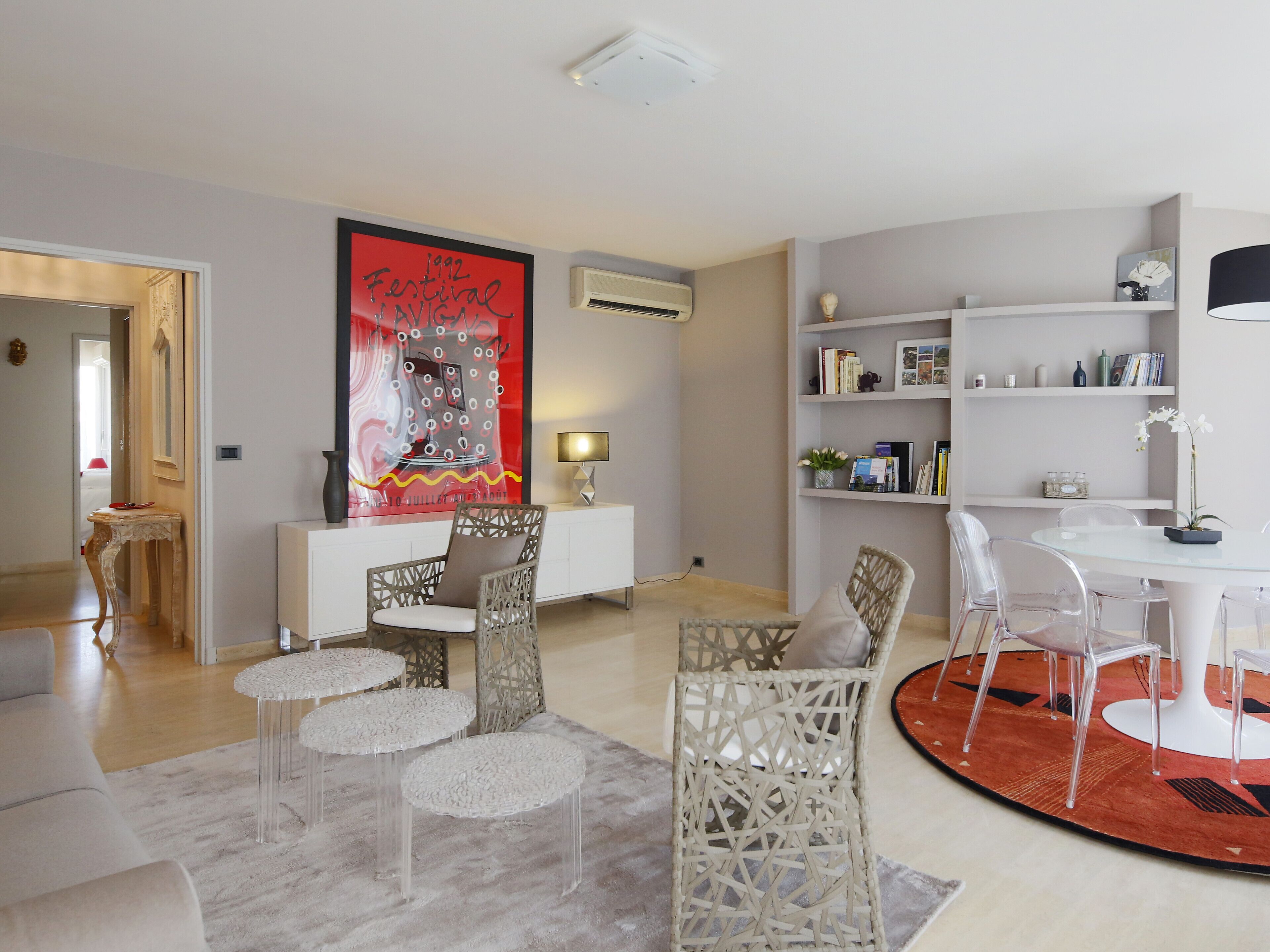 A modern living room with a round dining table, clear chairs, a white sofa, and a decorative rug.