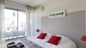 A hotel room with a bed, two red pillows, a white headboard, a bedside table with a lamp, a window with curtains, and a wall-mounted plant display.