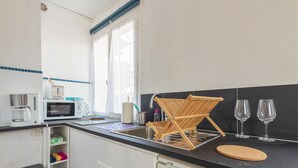 A compact kitchen with a microwave, toaster, and coffee maker. There is a wooden drying rack and two wine glasses on the counter. - Studio Bruscia - Welkeys (Six-Fours-les-Plages)