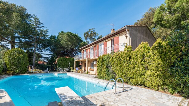 A swimming pool with stone tiles, a lounge area with chairs, and a building with a balcony. - Studio Bruscia - Welkeys (Six-Fours-les-Plages)