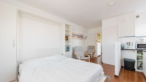 A bedroom with a bed, a chair, a desk, and a kitchenette. - Studio Bruscia - Welkeys (Six-Fours-les-Plages)
