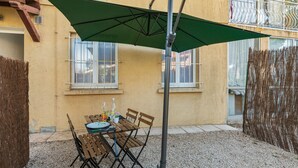 An outdoor patio with a table and chairs, a green umbrella, and a building in the background. - Studio Bruscia - Welkeys (Six-Fours-les-Plages)