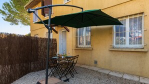 An outdoor patio with a table and chairs, a green umbrella, and a wooden fence. - Studio Varélia - Welkeys (Six-Fours-les-Plages)