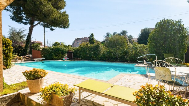 A swimming pool with a stone deck, surrounded by greenery and a metal table with chairs. - Studio Varélia - Welkeys (Six-Fours-les-Plages)
