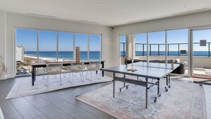 Une pièce spacieuse avec une table de ping-pong, de grandes fenêtres donnant sur la plage et un balcon avec des sièges d’extérieur.