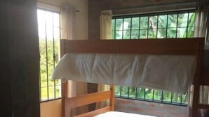 Ein Stockbett in einem Zimmer mit Blick auf grüne Natur durch vergitterte Fenster.