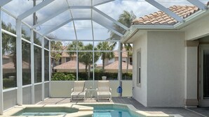 Una piscina exterior cubierta con sillones de descanso y un jacuzzi, rodeada por un muro blanco y vistas a palmeras y casas.