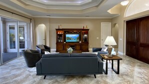 Un salón amplio con una televisión de pantalla plana grande, asientos cómodos e iluminación empotrada en el techo.