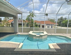 En inomhuspool med kristallklart blått vatten, omgiven av en glasvägg, och utsikt över bostadshus i bakgrunden.