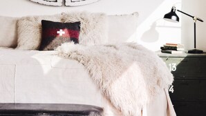 Un dormitorio con una gran decoración circular en la pared, una cama con una manta blanca y esponjosa, un plaid de piel sintética y una mesita de noche con libros y una lámpara.