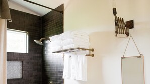 Un baño moderno con ducha revestida de baldosas oscuras, un lavamanos blanco y un salpicadero geométrico, y toallas ordenadas en un toallero.