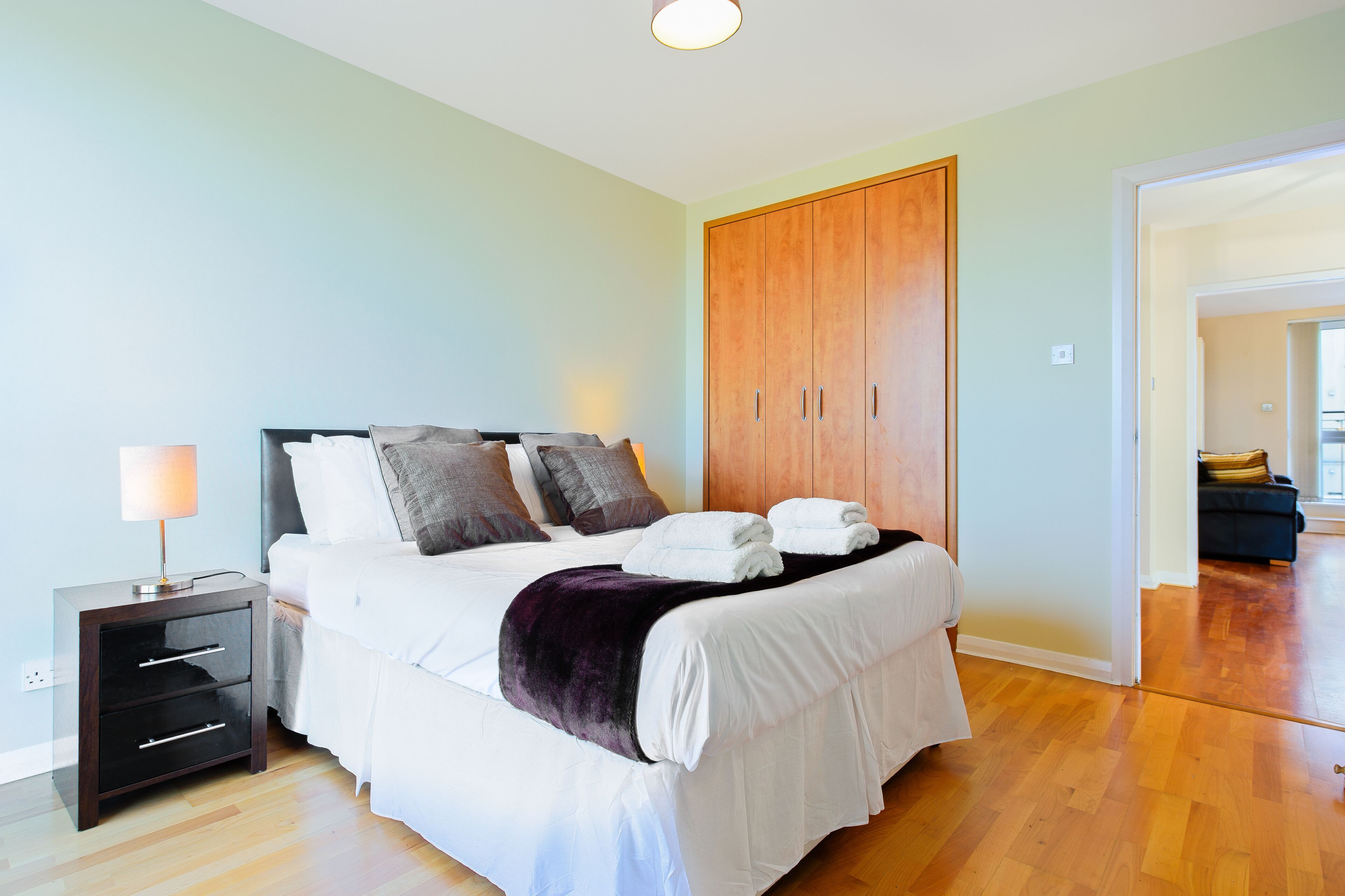 Een slaapkamer met een bed, nachtkastje, kledingkast en uitzicht op een andere kamer.
