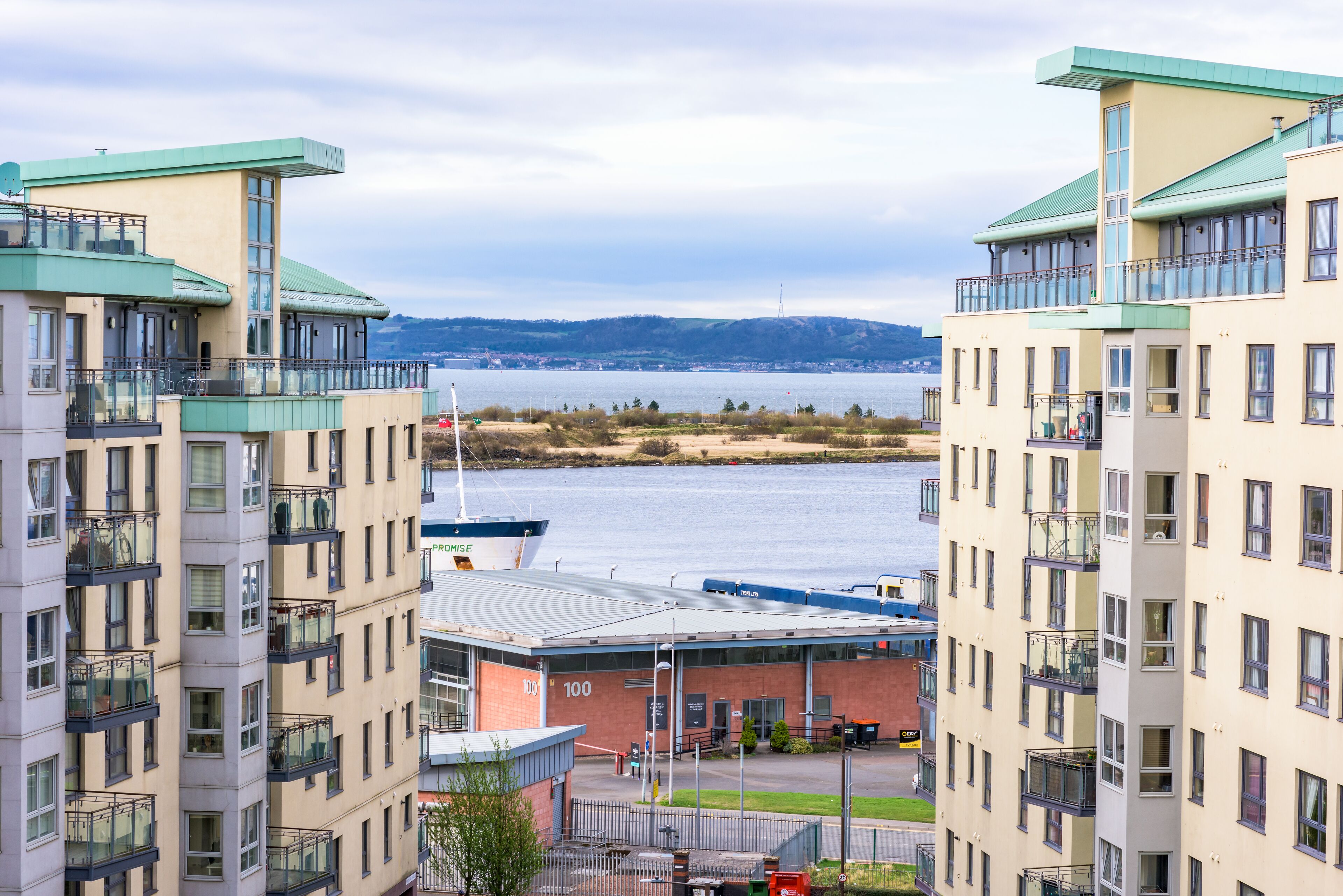 A modern hotel with multiple balconies, a view of the water, and a distant mountain range.