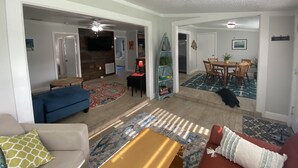 A spacious living room with a blue sofa, a red couch, and a yellow coffee table. There is a dining area with a wooden table and chairs, and a kitchen area with a refrigerator and a stove. - Rock Ridge I. Private and close to everything. (Vero Beach)