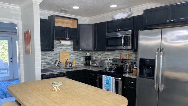 A modern kitchen with dark cabinets, stainless steel appliances, a wooden island, and a view to the outdoors. - Rock Ridge I. Private and close to everything. (Vero Beach)