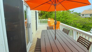 A wooden deck with a table and chairs, an orange umbrella, and a white railing.